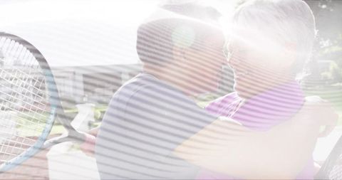 Sunlit senior couple embracing on backyard bench with tennis racket and joyful affection