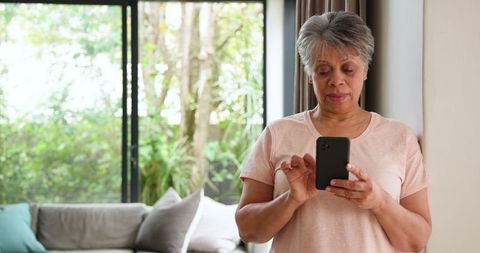 Senior Woman Relaxing with Smartphone Near Sunny Window at Home