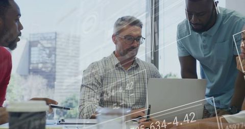 Multicultural team analyzing data on laptop with digital charts overlay in modern office