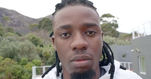 African American man standing on balcony wearing white hoodie with dreadlocks close-up