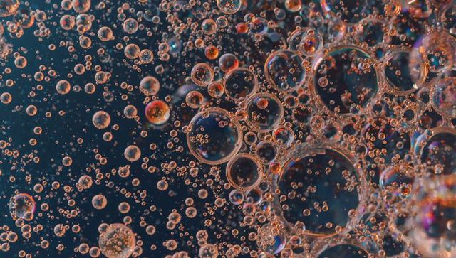 Macro oil droplet cluster with iridescent rings, amber-blue microbubbles and abstract bokeh