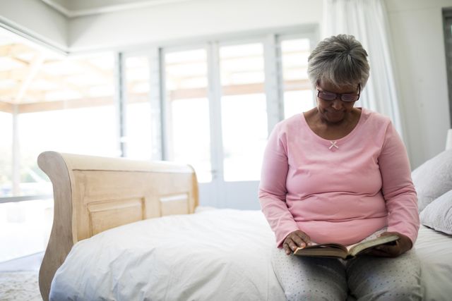 Senior woman reading book while sitting on bed in the bed room at home