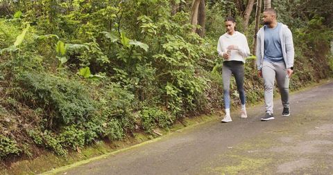 Couple walking on mossy forest trail in activewear holding travel mug and water bottle