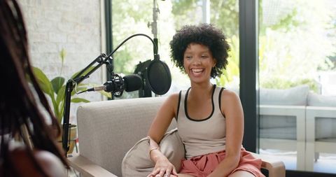 African american women cohosting podcast laughing on couch in bright home studio