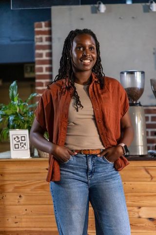 Smiling african barista standing behind cafe counter wearing rust shirt and jeans
