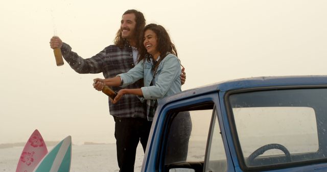 Young Caucasian man and biracial woman celebrate outdoors, with copy space. They're enjoying a champagne spray by their car after a surfing session.