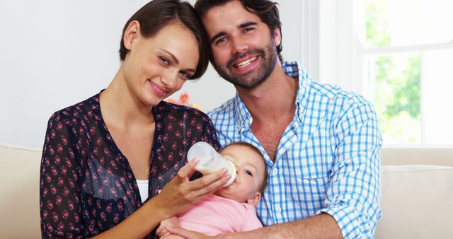 Happy Young Parents Feeding Baby with Milk Bottle in Living Room - Download Free Stock Images Pikwizard.com