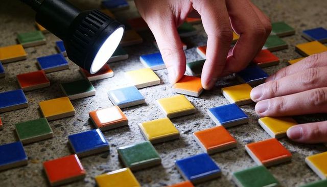 Crafting colorful ceramic tile mosaic with hands and flashlight on mortar bed, closeup
