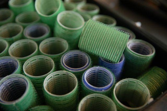 Close up of multiple rows of green and blue hair rollers prepared for curling hair hair in hair salon. Hair and beauty treatment service.