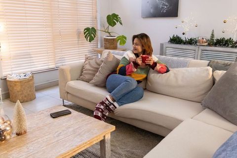 Woman relaxing on sectional sofa holding red mug in cozy neutral living room