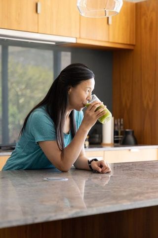 Asian woman drinking green smoothie at modern marble kitchen island morning routine