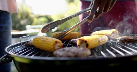 Men grilling corn and burgers on backyard charcoal grill