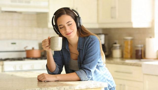 Woman relaxing with mug and over-ear headphones at bright marble kitchen island