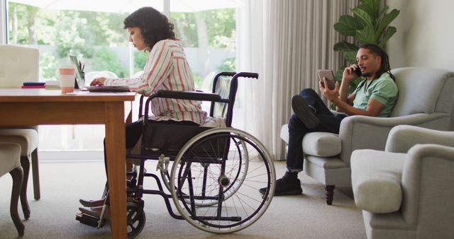 Young woman in wheelchair working at home office while young man watches tablet - Download Free Stock Images Pikwizard.com