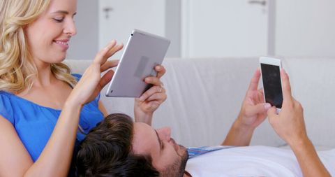 Relaxed Couple Engaging with Devices on Sofa at Home