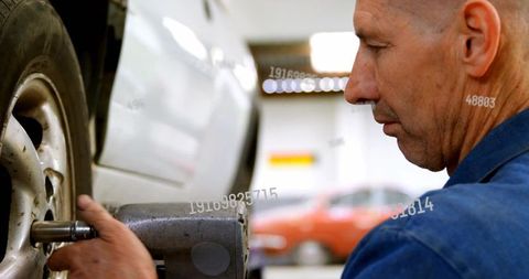 Mechanic tightening car wheel using pneumatic impact wrench in modern auto repair workshop