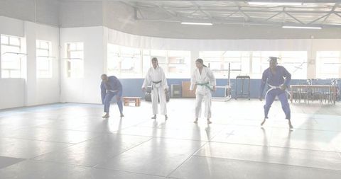 Practicing judo class performing stepping drills in bright dojo wearing gis and colored belts