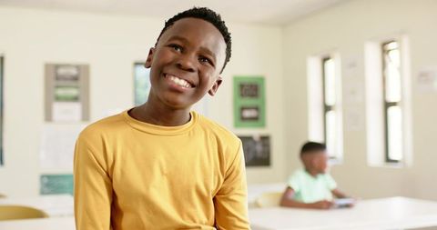 Smiling african american boy sitting in bright classroom wearing yellow shirt