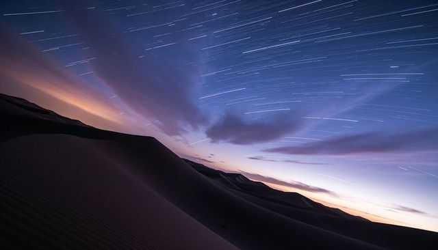 Starlit desert dunes with long-exposure star trails, rippling ridges and twilight sky