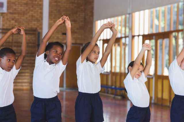 Group of school children stretching in a gym during a physical education class. Ideal for educational materials, health and fitness promotions, and youth activity programs.
