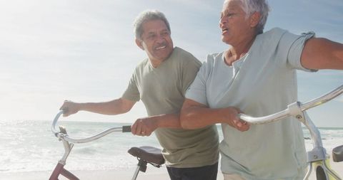 Elderly Hispanic Couple Strolling with Bicycles on Beach at Sunset