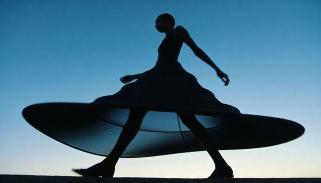 Silhouetted woman walking in dramatic circular skirt at sunset, editorial fashion motion and grace