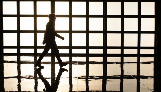 Silhouette man walking across glossy atrium floor reflecting backlit square window grid and shadows
