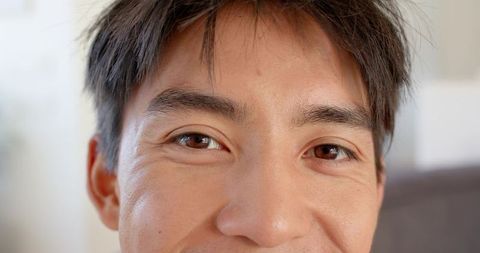 Serene closeup of asian man making eye contact and smiling subtly on sofa in natural light
