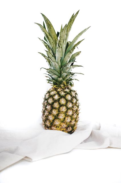 Close-up of a fresh pineapple resting on white cloth against a white background. Ideal for use in healthy eating and lifestyle blogs, food-related advertisements, natural food promotions, or tropical-themed marketing materials.