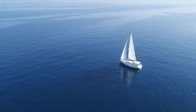 Sailing white yacht gliding across calm open ocean with tall mast and mirror reflection