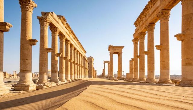 Sunlit ancient colonnade stretching through desert avenue showing rippled sand and stone gateway