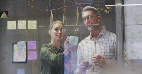 Team brainstorming on glass wall with sticky notes and data charts for strategic planning