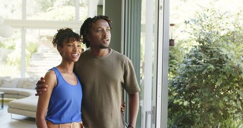 African american couple standing at sliding glass door looking toward sunlit garden