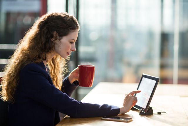 Businesswoman using digital table while having cup of coffee in office