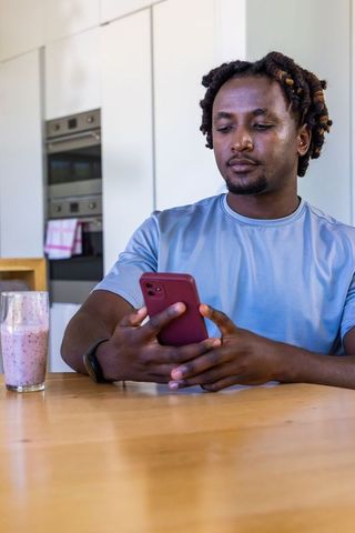 Man using smartphone while enjoying berry smoothie at minimalist modern kitchen table
