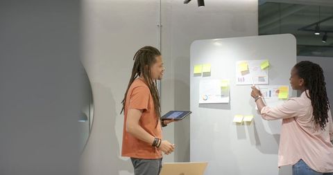 African coworkers brainstorming and pointing at charts on whiteboard while holding tablet