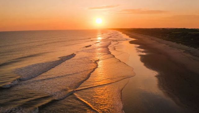 Golden sunset reflecting on wet sand and rolling waves along deserted coastline panorama