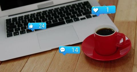 Red coffee cup beside laptop with social media notifications on wooden desk