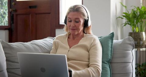 Mature woman relaxing at home with laptop and headphones
