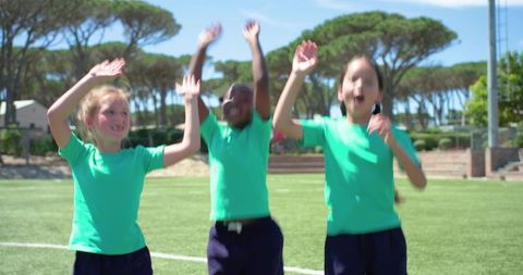 Multiracial schoolgirls jumping and cheering on sunny sports field in green shirts