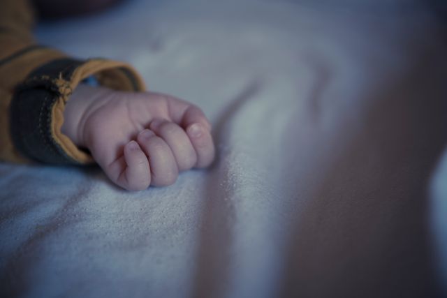 Newborn's hand delicately clenched on soft fabric, capturing the essence of innocence and tranquility. Ideal for use in parenting blogs, baby product advertisements, childcare educational materials, and maternity-related content.