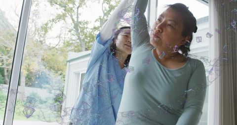 Home caregiver assisting senior with arm mobility exercise by sliding glass door with digital mesh