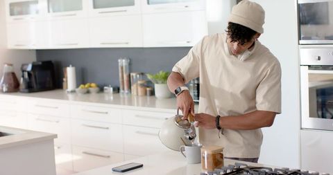 African american man pouring hot water into mug at modern white kitchen island