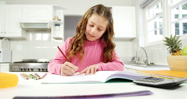 Young girl sits in kitchen working intensely on homework with colored pencils scattered around. Convenient, bright natural light from large windows emphasizes an educational focus. Enthusiastic learner in a home environment. Ideal for educational resource ads, homeschooling, children's learning tutorials.