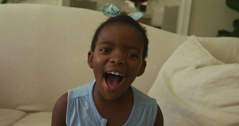 Joyful Young Girl with Hair Bow Laughs in Dimly Lit Room