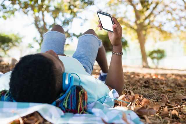 Young man using mobile phone while lying on a picnic blanket in the park