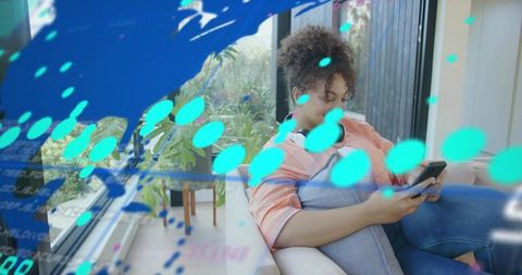 Casual woman on sofa using smartphone with augmented reality overlays and headphones