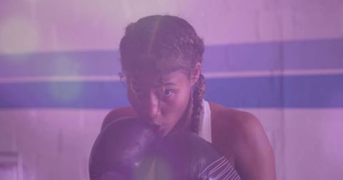 Woman boxer raising gloves in ring under purple light showing focus and intensity