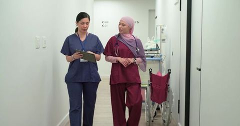 Diverse female nurses walking hospital corridor holding tablet and wearing stethoscope