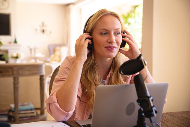 Woman wearing headphones working on laptop in home office. Ideal for illustrating remote work, online meetings, podcasting, and flexible working environments. Perfect for articles on work-life balance, home office setups, and modern communication technology.